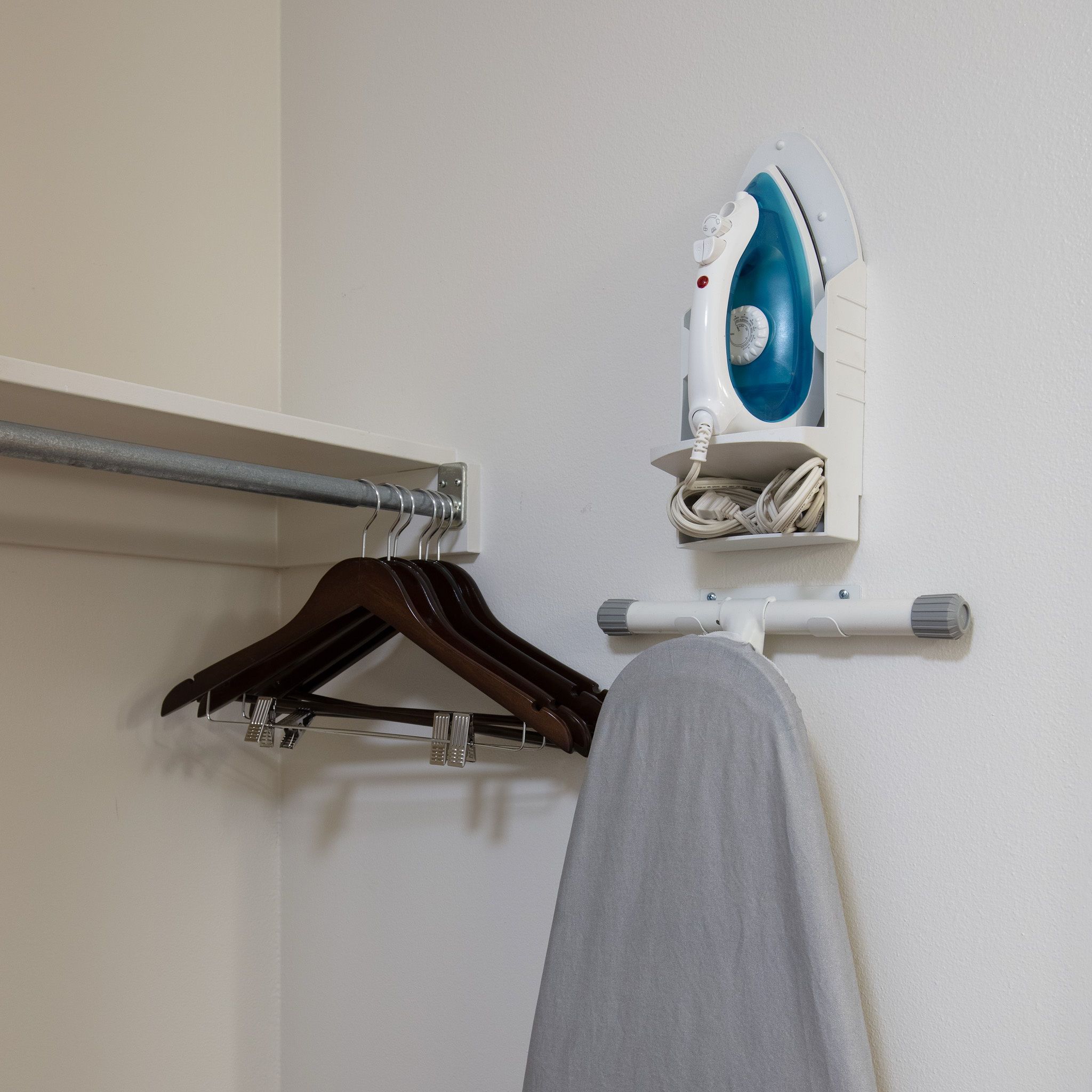 A wall-mounted ironing board with an iron, a metal towel rail, and a wooden hanger.