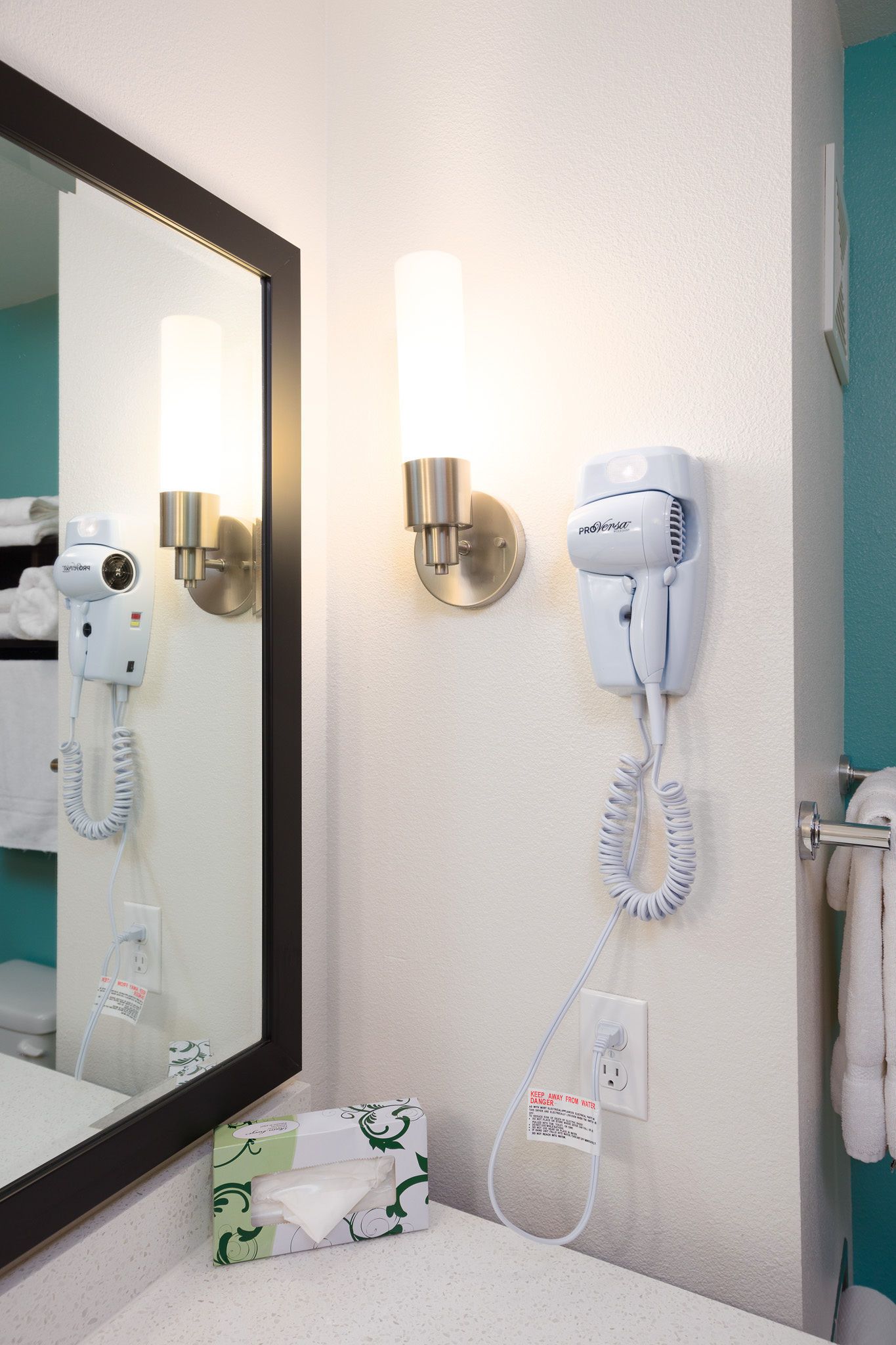 Une salle de bain d’hôtel équipée d’un sèche-cheveux fixé au mur, d’un porte-serviettes et d’un miroir.