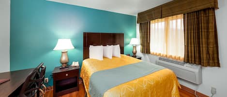 A hotel room with a bed, two bedside lamps, a desk with a chair, a heater, and a window with curtains.