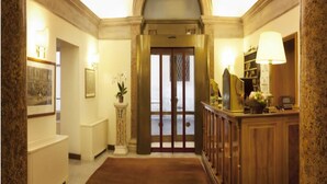 Um hall imponente com piso de mármore, um balcão de recepção e uma grande porta em arco.