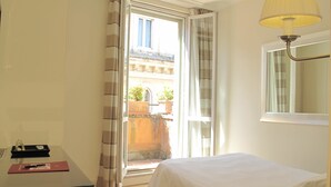 Quarto de hotel com cama, secretária, luminária e vista para a varanda.