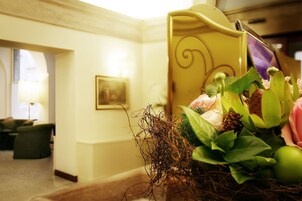 Een hotellobby met een receptiebalie, een ingelijst kunstwerk aan de muur en een bloemstuk op de balie.