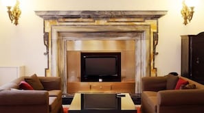 Een woonkamer met een open haard, een flatscreen televisie en twee banken met rode kussens.