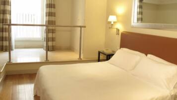 A hotel room with a bed, a nightstand, a lamp, a window with curtains, and a balcony.