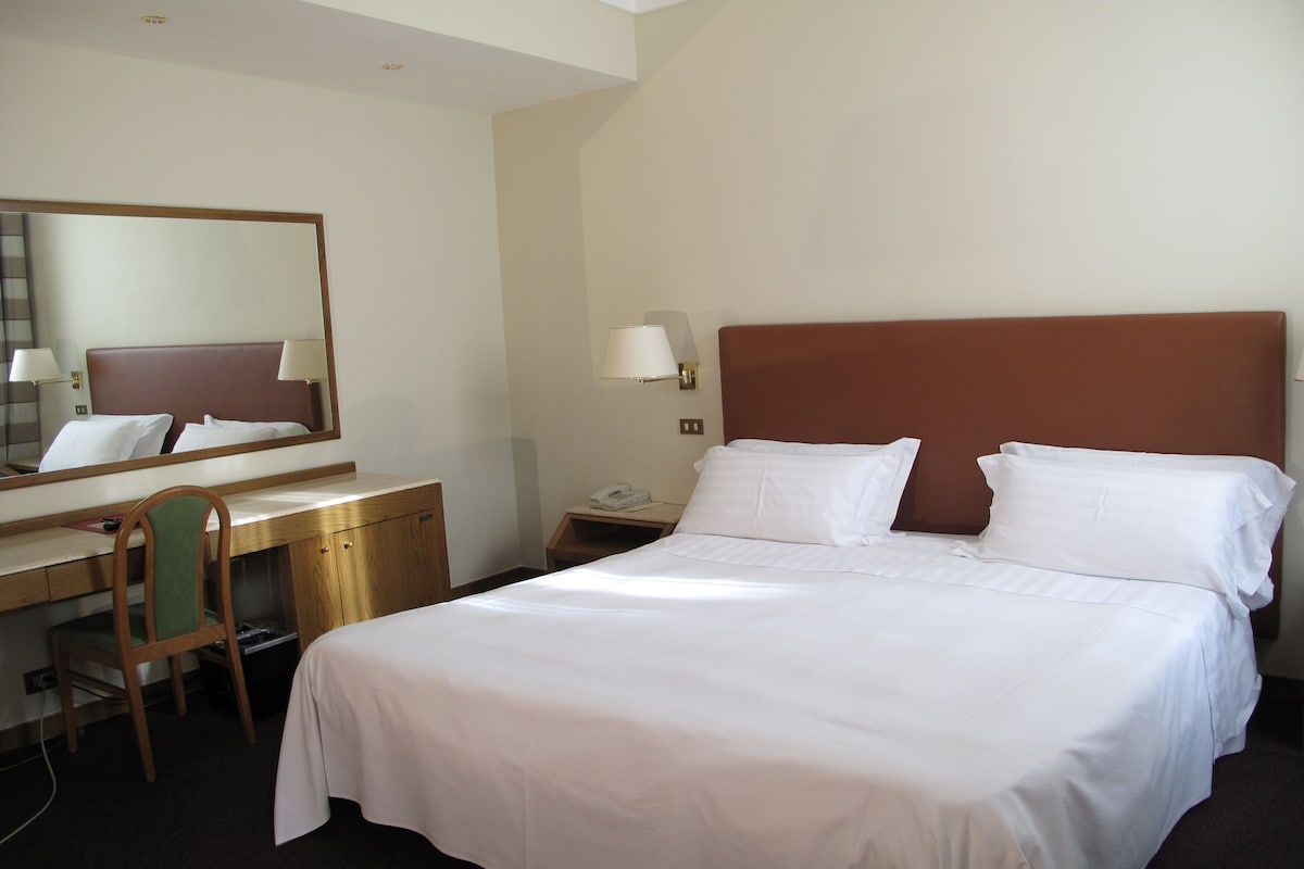 Een hotelkamer met een enkel bed, een bureau met stoel, een telefoon en een spiegel.