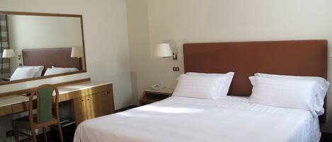 Una habitación de hotel con una cama individual, un escritorio con silla, un teléfono y un espejo.