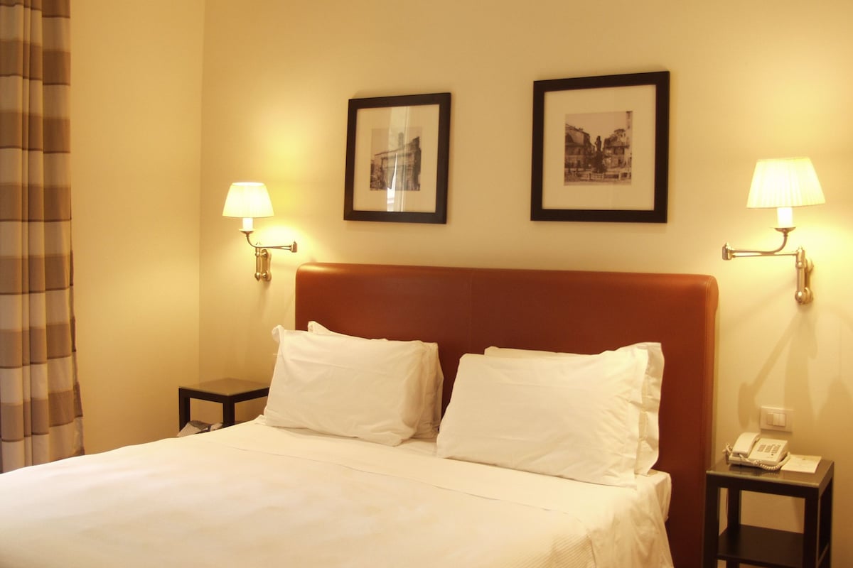 A hotel room with a bed, two bedside tables, two wall-mounted lamps, and two framed pictures on the wall.