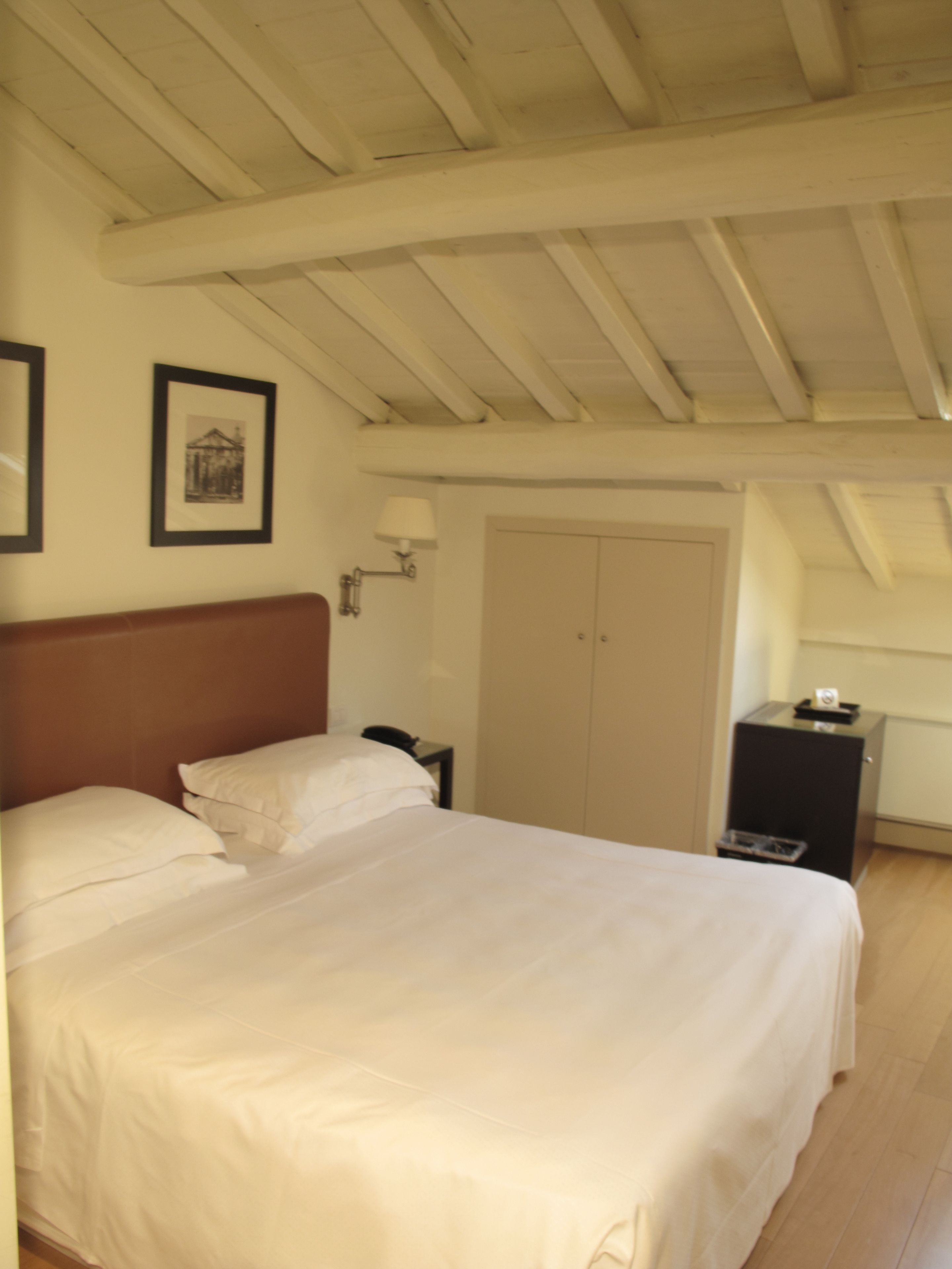 A bedroom with a large bed, a nightstand, a lamp, a wardrobe, and a framed picture on the wall.