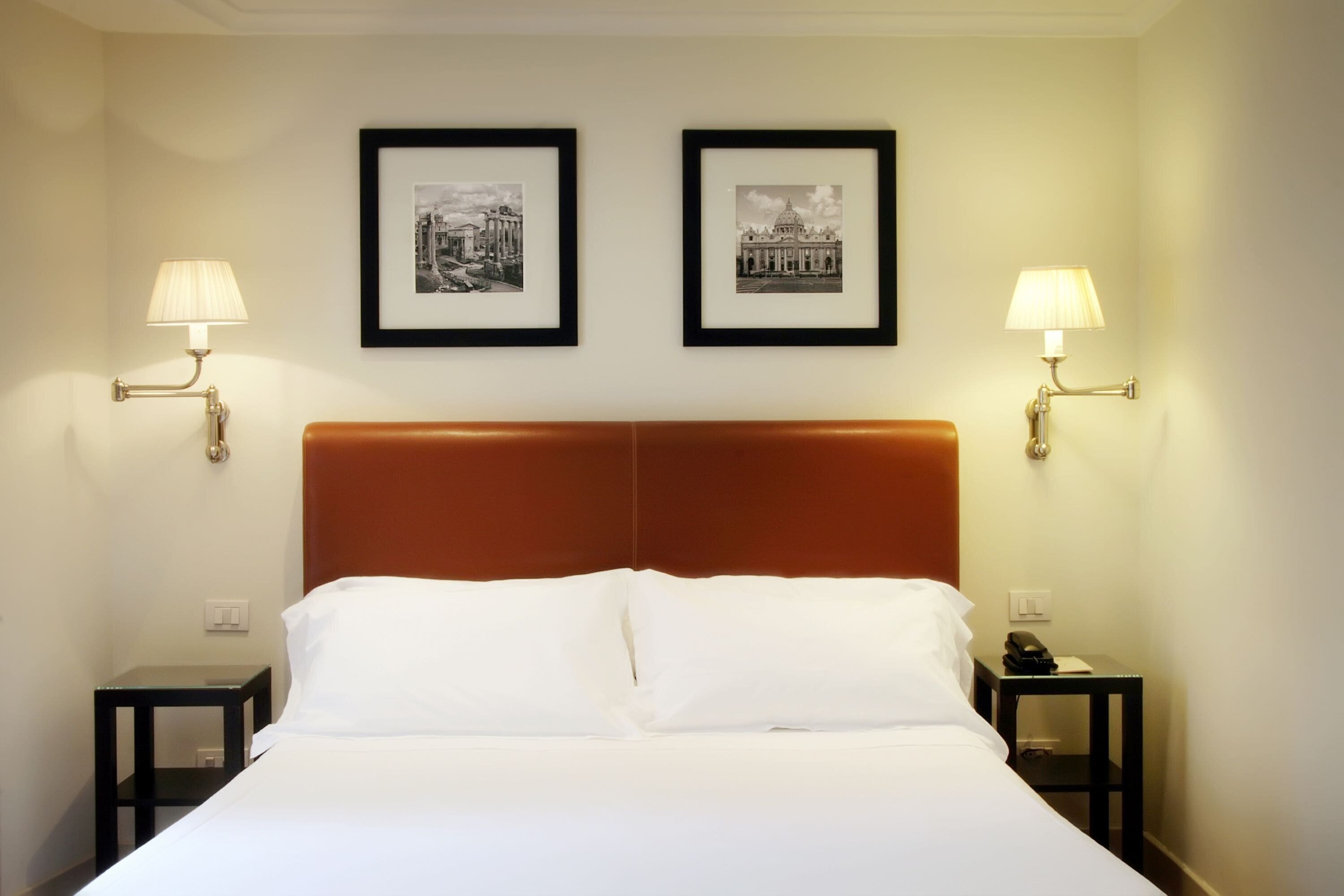 Quarto de hotel com uma cama grande, duas mesinhas de cabeceira e duas luminárias fixadas na parede.