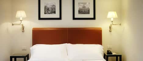 Quarto de hotel com uma cama grande, duas mesinhas de cabeceira e duas luminárias fixadas na parede.