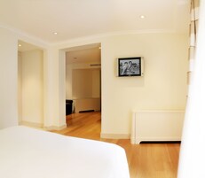 A hotel room with a large bed, wooden flooring, a white radiator, and a framed picture on the wall.
