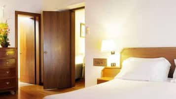 A hotel room with a wooden wardrobe, a bedside table with a lamp, and a bed with white linens.
