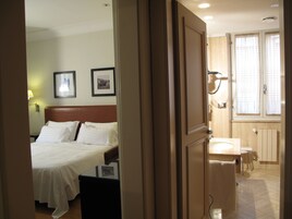 Una camera d'albergo con un letto, un comodino, una lampada a parete e un bagno con lavandino e wc.
