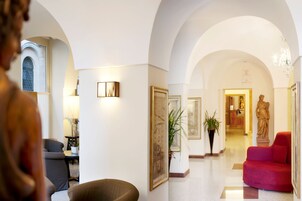 Un hall d’hôtel doté de plafonds en arc de cercle, d’un canapé rouge, d’une statue et d’œuvres d’art encadrées accrochées aux murs.