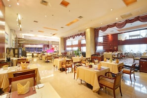 A spacious hotel dining area with multiple tables and chairs, a central bar, and large windows allowing natural light. - Grand Royal Hotel (Guangzhou)