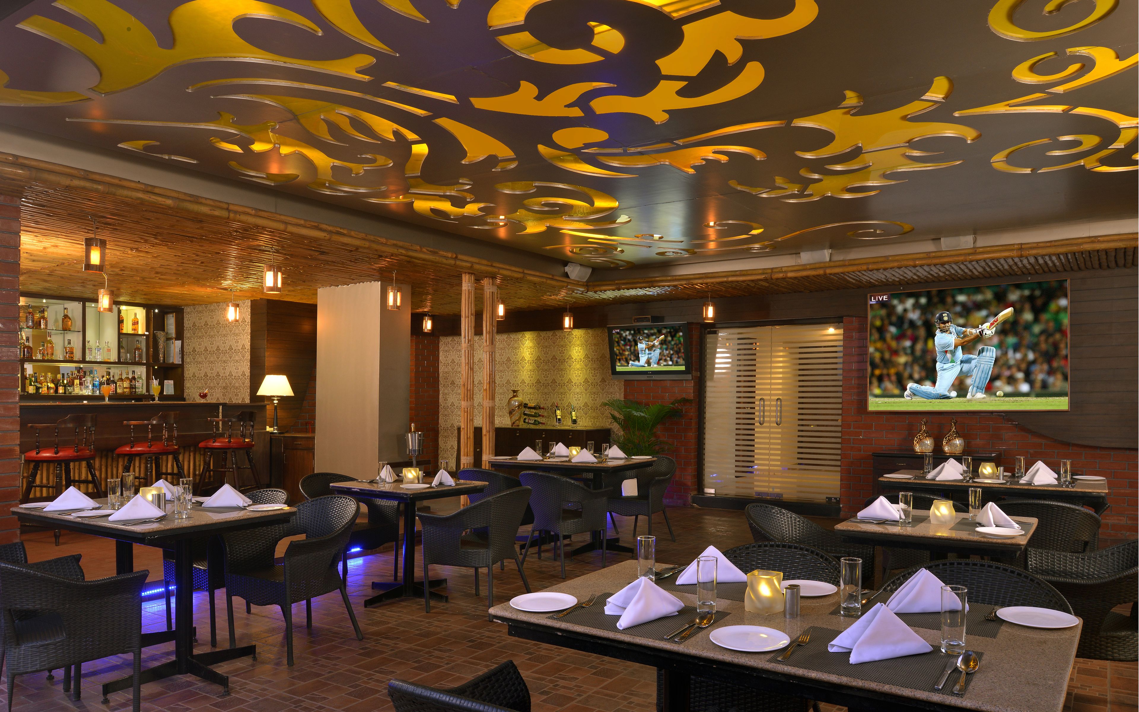 A restaurant with multiple tables set for dining, a bar area with bottles, and a television screen displaying a sports event.