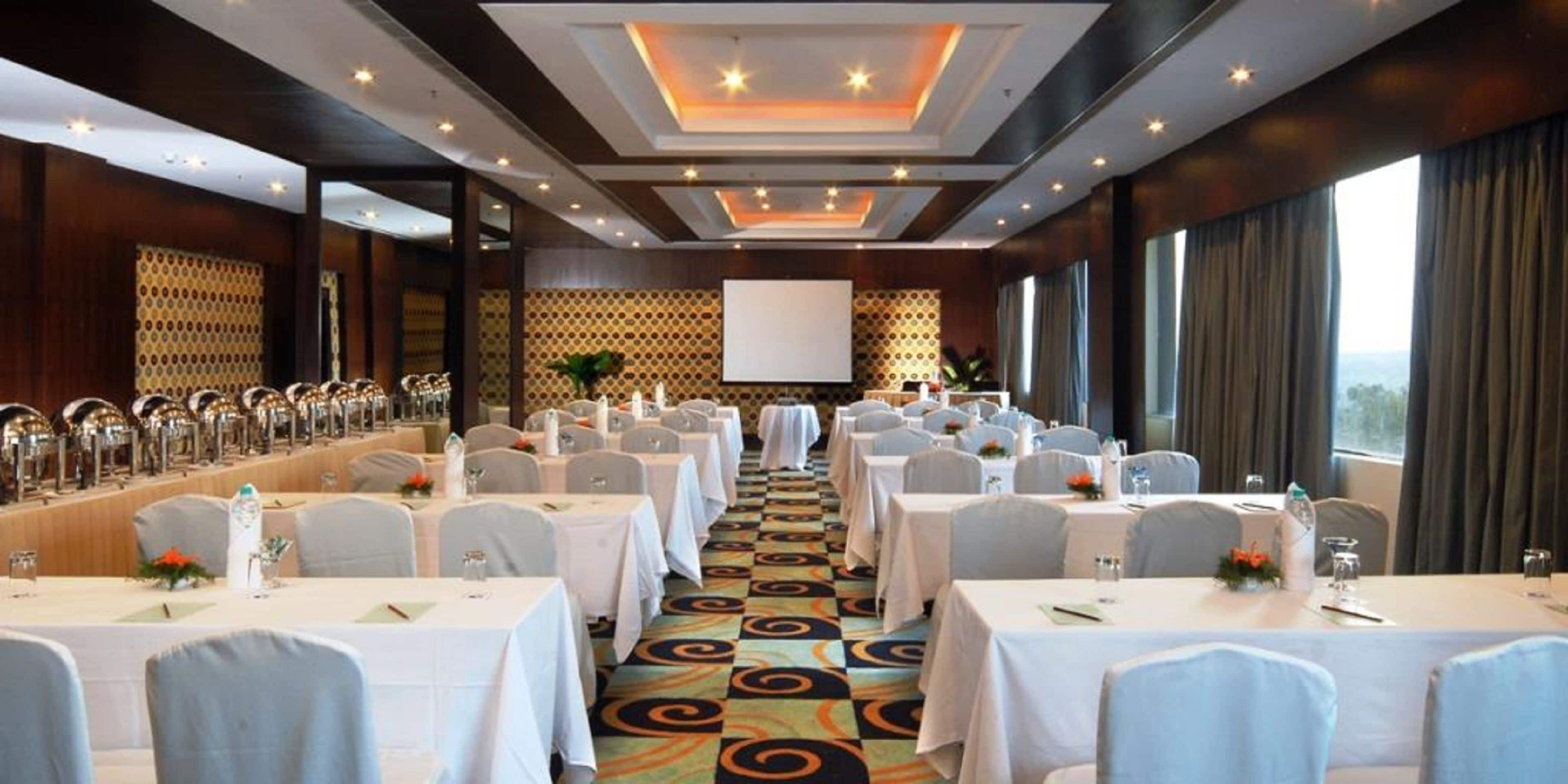 A conference room with rows of tables, a projector screen, and a patterned carpet.
