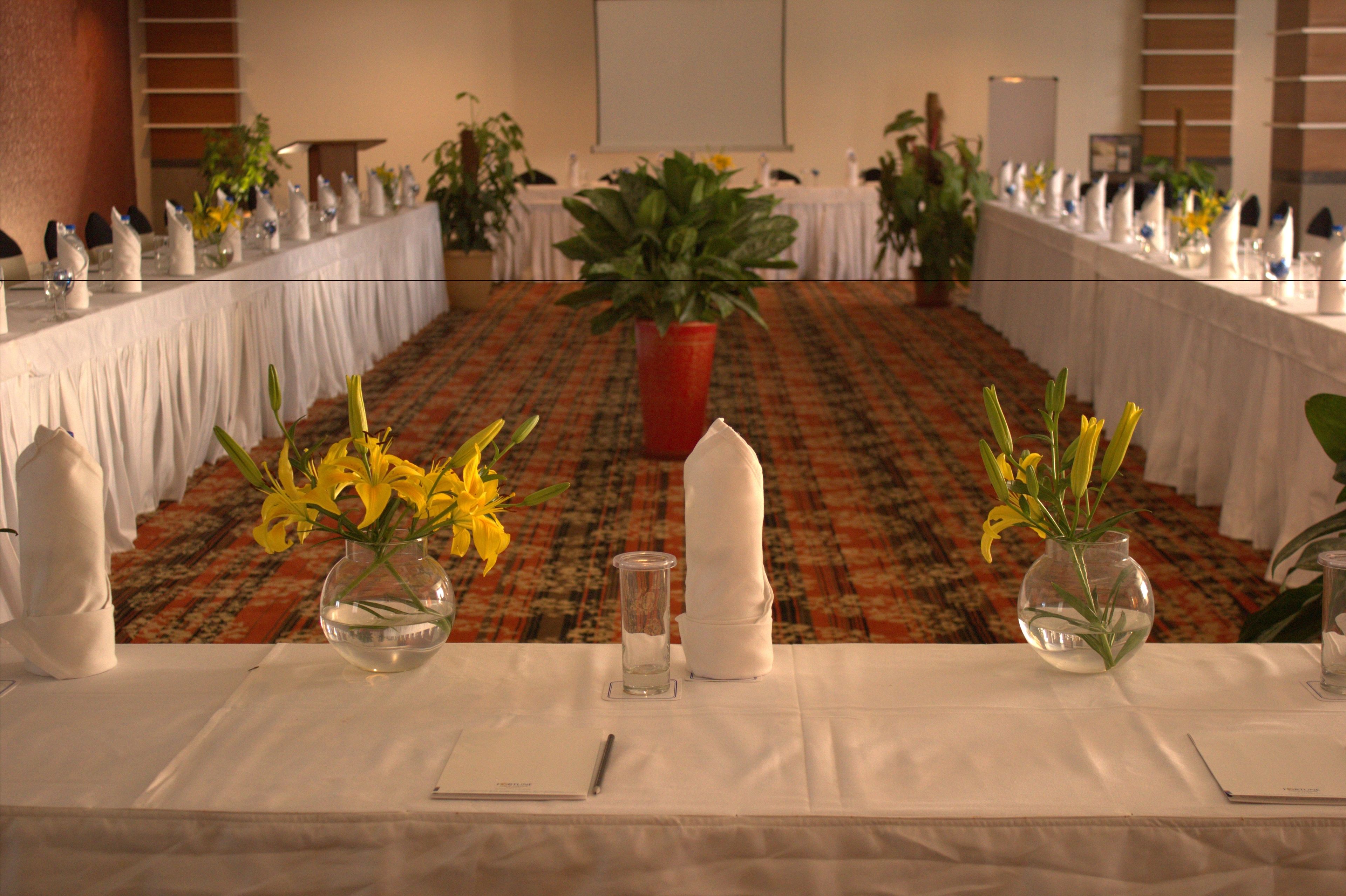 A banquet hall with long tables set for a formal event, featuring floral centerpieces and white tablecloths.