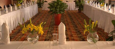 Ein Festsaal mit langen Tischen, gedeckt für eine festliche Veranstaltung, mit floralen Mittelpunkten und weißen Tischdecken.