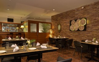 Un restaurante con varias mesas dispuestas para comer, una zona de bar con una variedad de botellas y una pared decorativa con un espejo circular y una obra de arte texturizada.