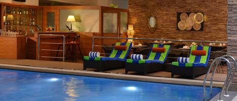 Un área junto a la piscina con sillones de descanso, un bar y un comedor.