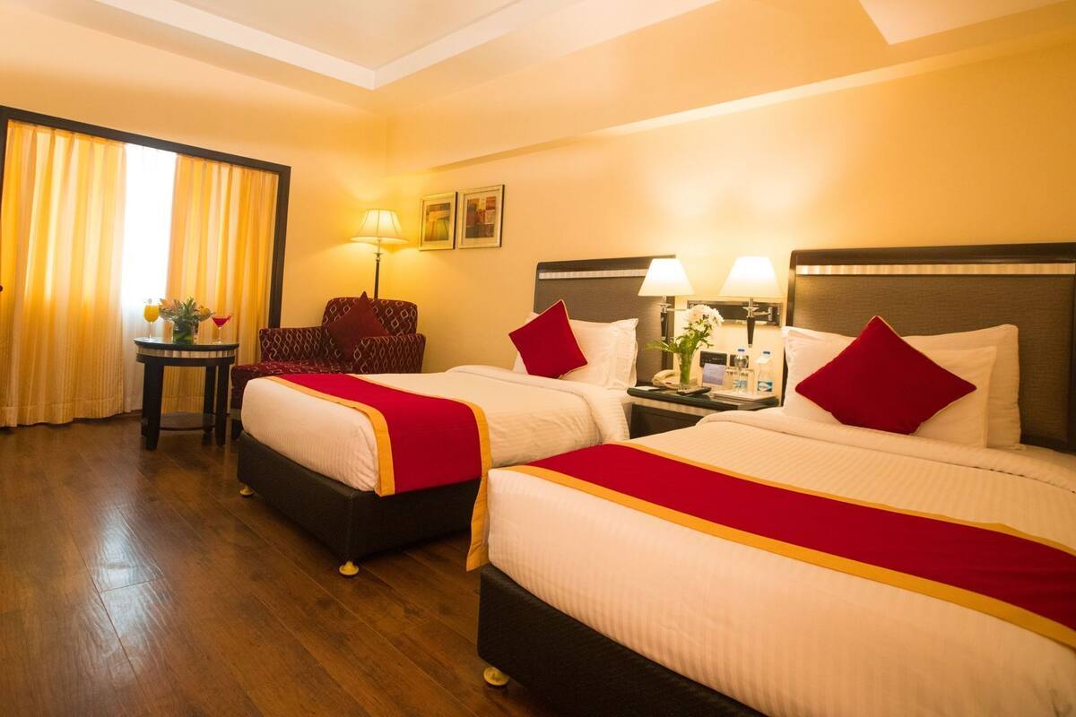 A hotel room with two beds, a desk, a chair, and a window with curtains.