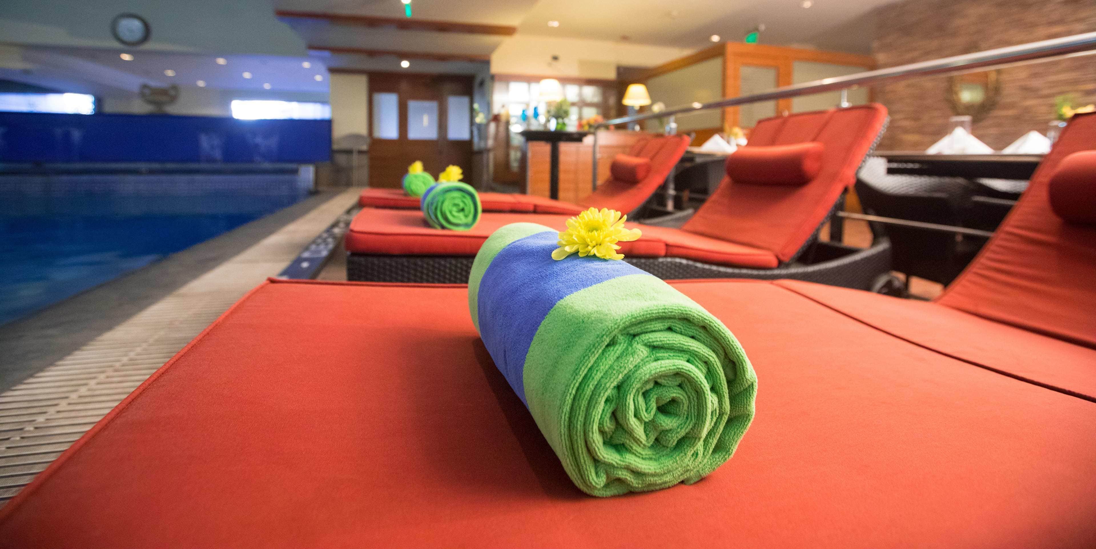 A poolside area with red lounge chairs, a pool, and a towel with a flower.
