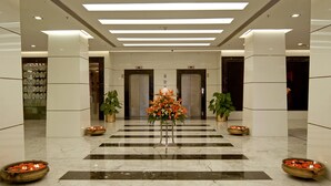 Un hall d’entrée avec un sol en marbre, deux plantes en pot, une composition florale et deux vases remplis de fleurs.