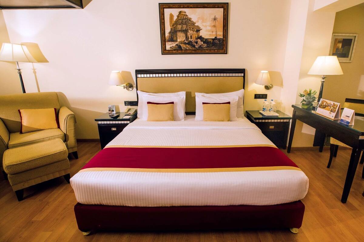 A hotel room with a large bed, a chair, a desk, and a painting on the wall.
