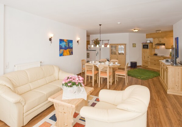 A modern living room with a beige sofa, a wooden coffee table with a vase of flowers, and a dining area with wooden chairs and a table. - Appart- und Wellnesshotel Charlotte (Seefeld in Tirol)