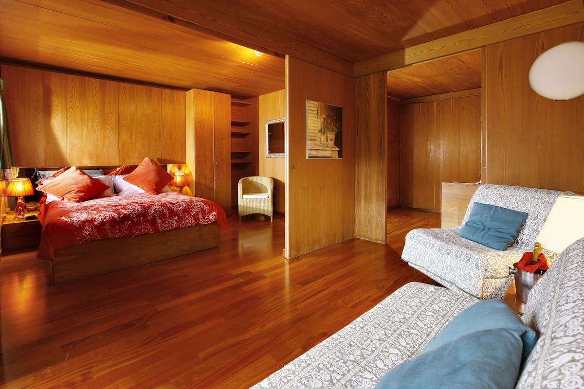 A wooden-floored bedroom with a bed, a chair, and a sofa.