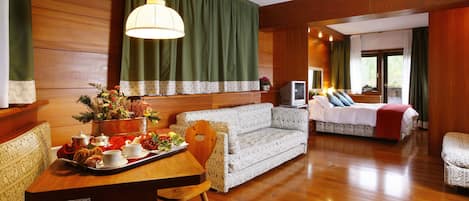 Une chambre d’hôtel avec un plancher en bois, un canapé, une table à manger sur laquelle se trouve un plateau de nourriture et un téléviseur.