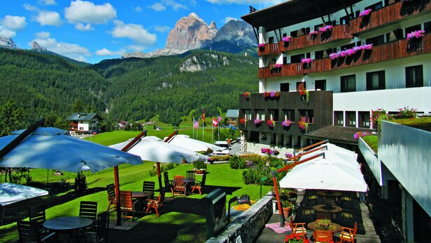 A hotel with outdoor seating, a mountain view, and balconies with flowers. - Hotel Mirage (Cortina d'Ampezzo)