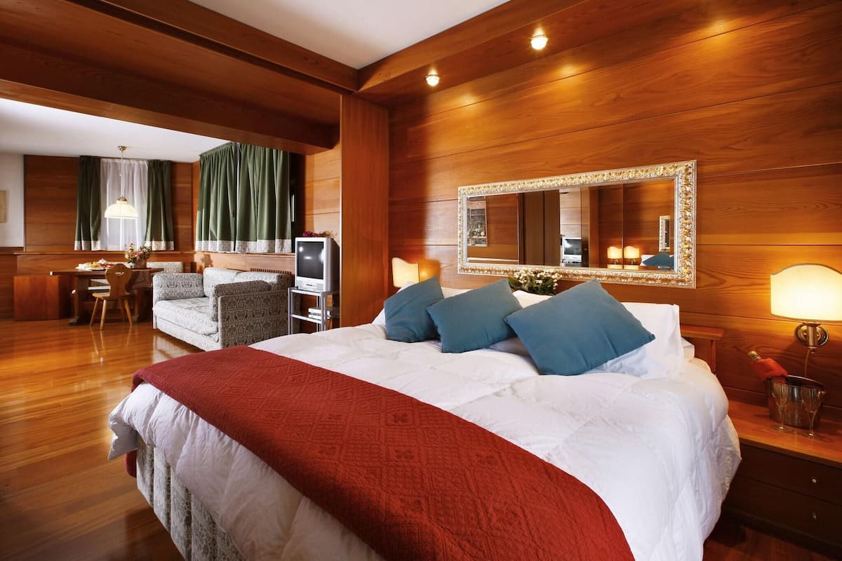 A hotel room with a large bed, a desk with a computer, a chair, and a mirror on the wall.