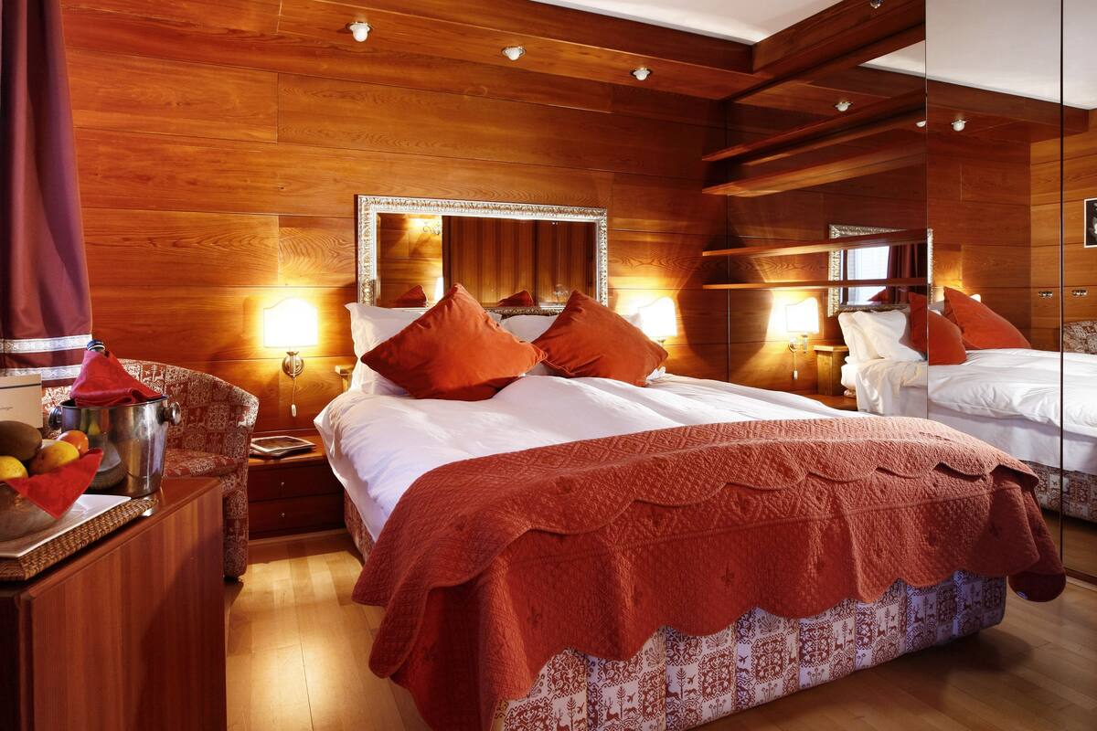 A hotel room with a large bed, wooden paneling, and a mirror above the bed.