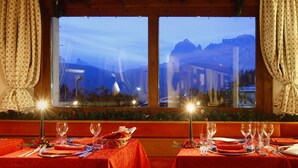 A dining area with tables set for a meal, a window with a view of mountains, and a festive wreath on the windowsill. - Hotel Mirage (Cortina d'Ampezzo)