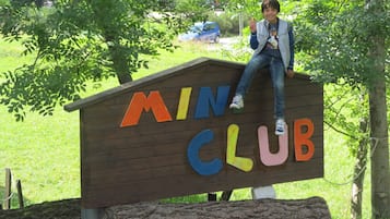 Een houten bord met kleurrijke letters waarop 'MINI CLUB' staat, in een park.