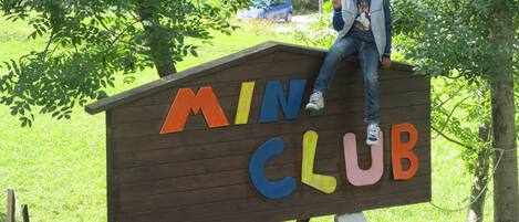 A wooden sign with colorful letters spelling "MINI CLUB" in a park setting.