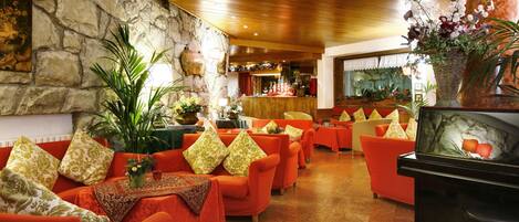 A hotel lobby with orange sofas, a stone wall, a wooden ceiling, and a bar area.