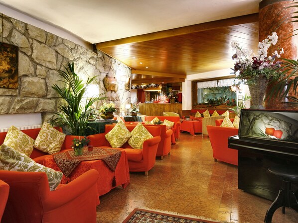 Un vestíbulo de hotel con sofás naranjas, una pared de piedra, un techo de madera y una zona de bar.