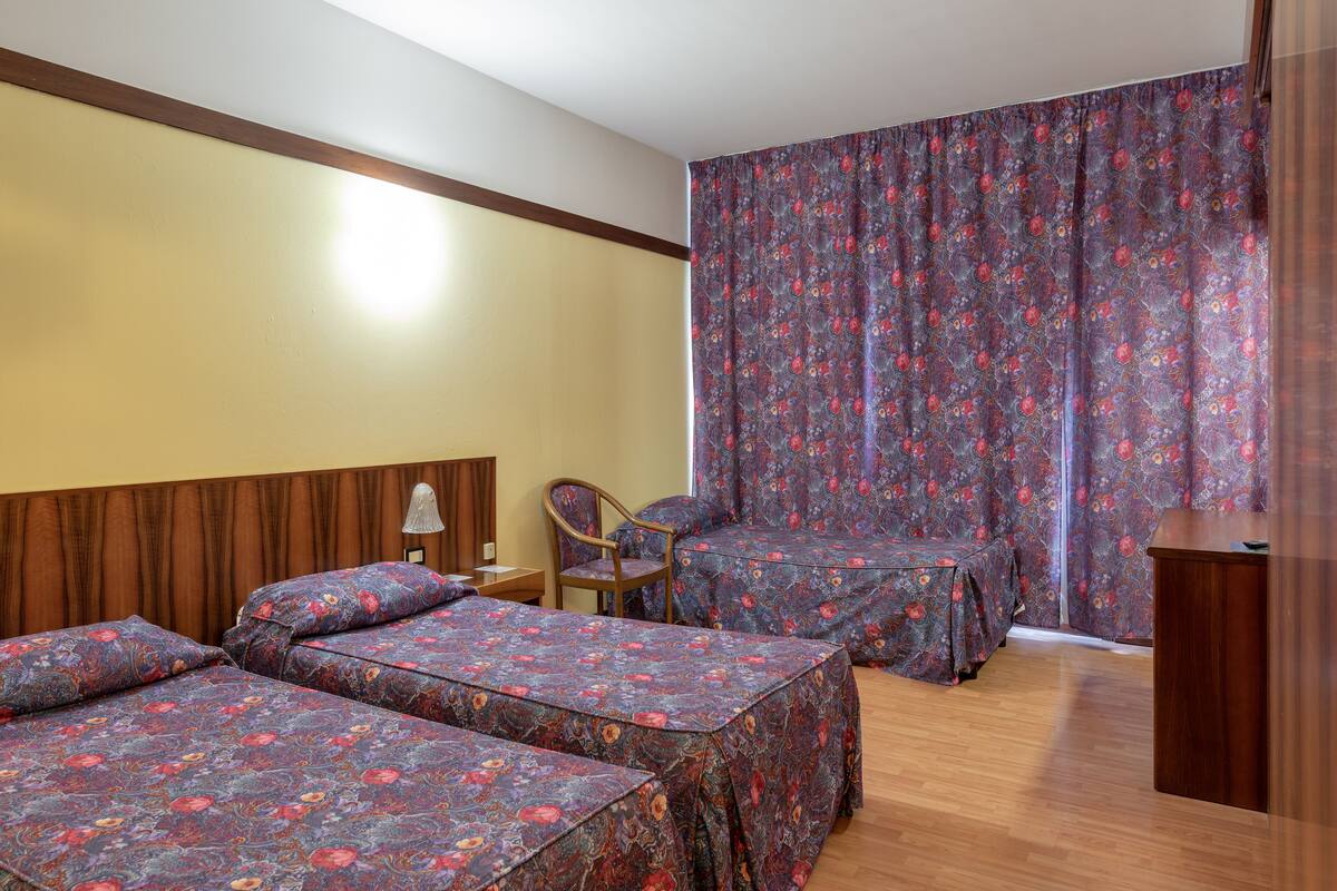 Ein Hotelzimmer mit zwei Einzelbetten, einem Holzkopfteil, einem Schreibtisch und einem Stuhl.