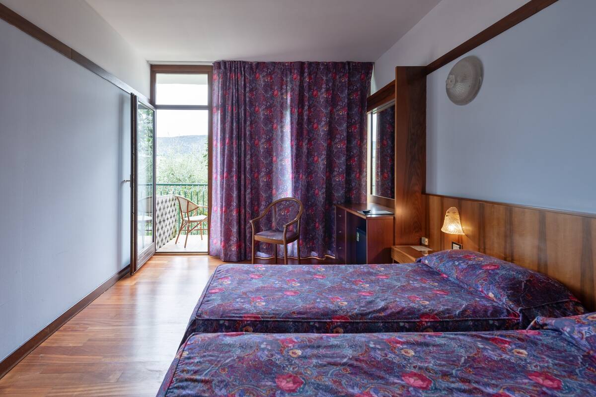 Ein Schlafzimmer mit einem großen Bett, einem Sessel, einem Schreibtisch und einem Fenster mit Vorhängen.