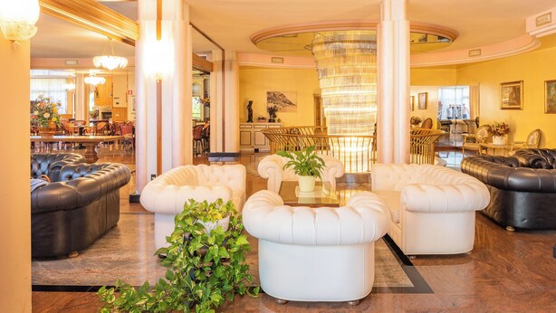 A spacious lobby with a central seating area, a chandelier, and a staircase leading to an upper level. - Park Hotel Oasi (Garda)