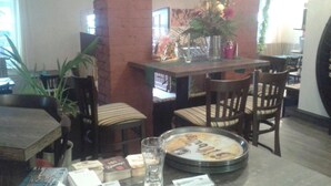 Un comedor con pared de ladrillo, sillas de madera, una mesa con mantel individual y un florero con flores.