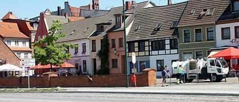Une vue de rue avec des bâtiments européens traditionnels, un ciel dégagé et un fourgon garé.