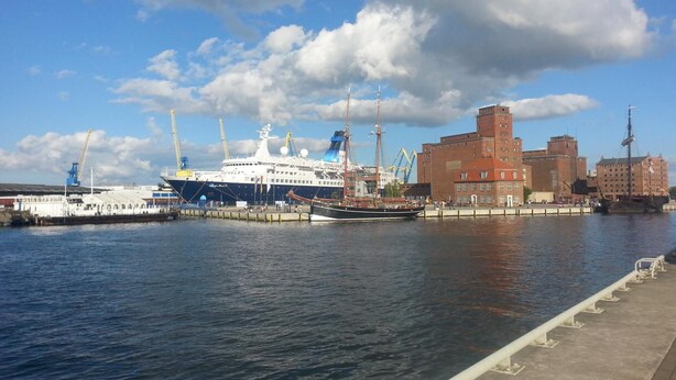 Un puerto con un gran crucero amarrado, un muelle y edificios industriales.
