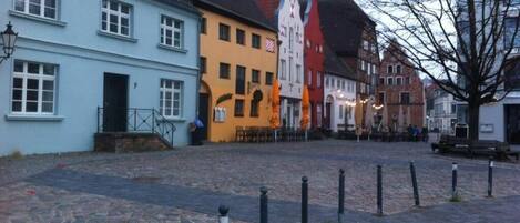 A cobblestone street with historic buildings, a bench, and bollards.