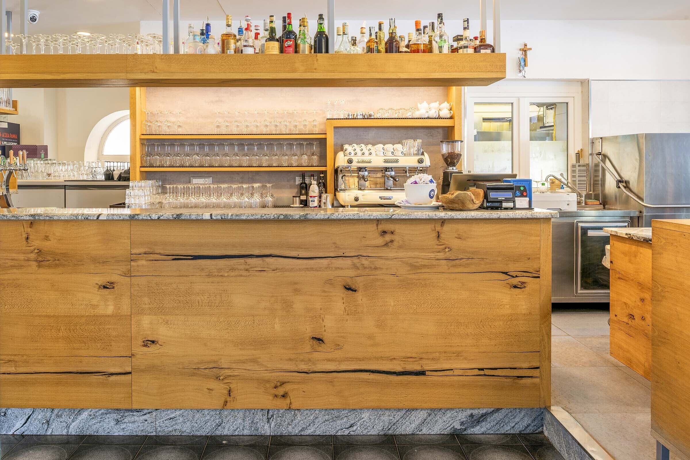 Een bar met een houten toonbank, planken met glazen en flessen, en een koffieapparaat.
