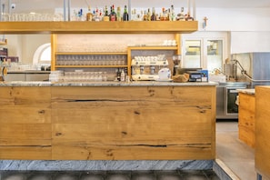 A bar area with a wooden counter, shelves with glasses and bottles, and a coffee machine. - Hotel Malcesine (Malcesine)
