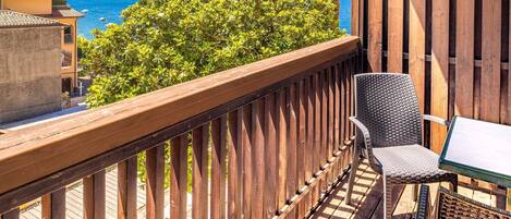 A balcony with a wooden railing, a wicker chair, and a table.
